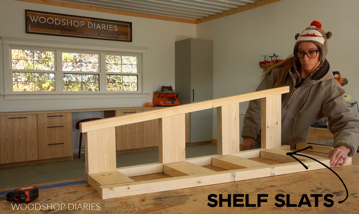 Shara Woodshop Diaries dry fitting corner shelf pieces together on workbench in workshop with an arrow pointing to shelf slat pieces for clarification