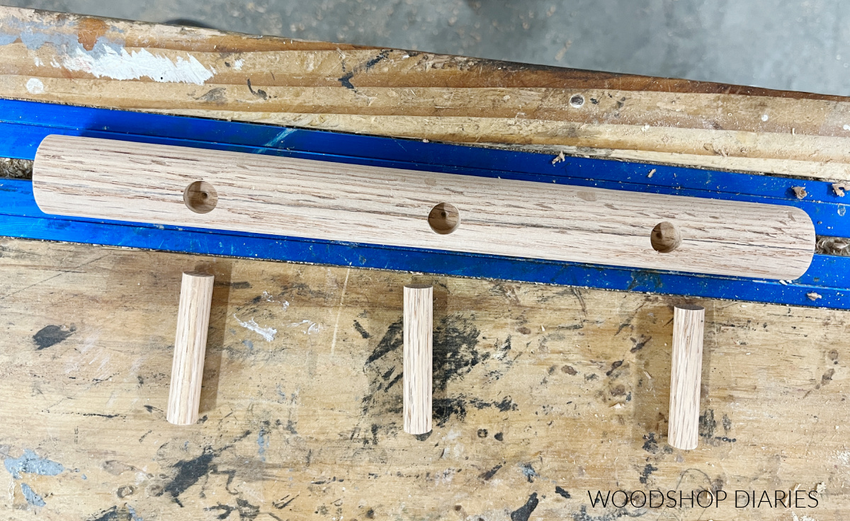 Large wooden dowel with three peg holes drilled out with smaller dowel pins cut to length for mug holder