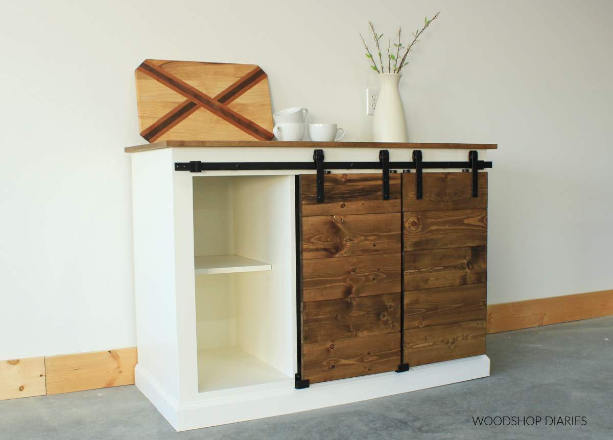 Completed DIY sliding door cabinet painted white with stained wood slatted doors covering two of the three sections--left side open