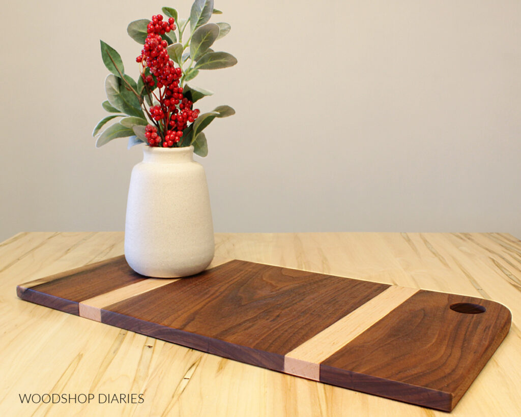 Two tone cutting board--walnut and maple sitting on table with vase