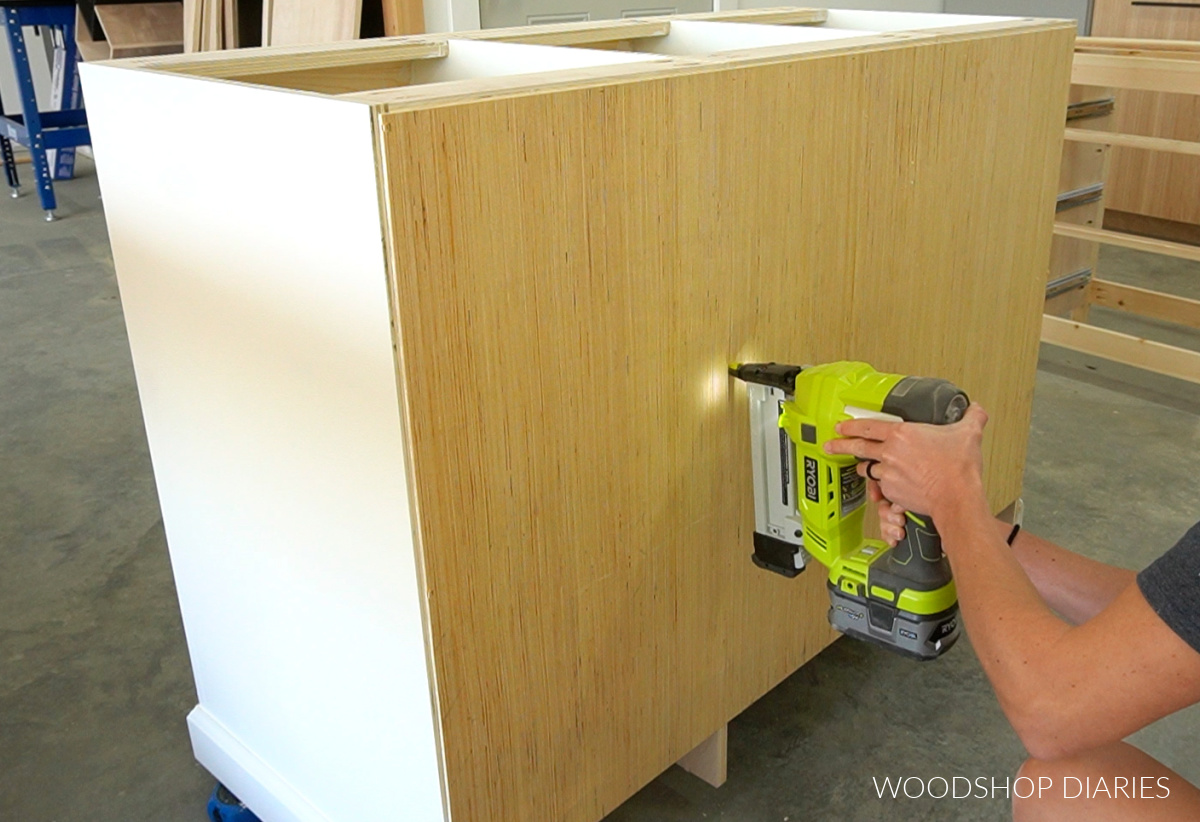 Shara Woodshop Diaries stapling back panel onto white cabinet