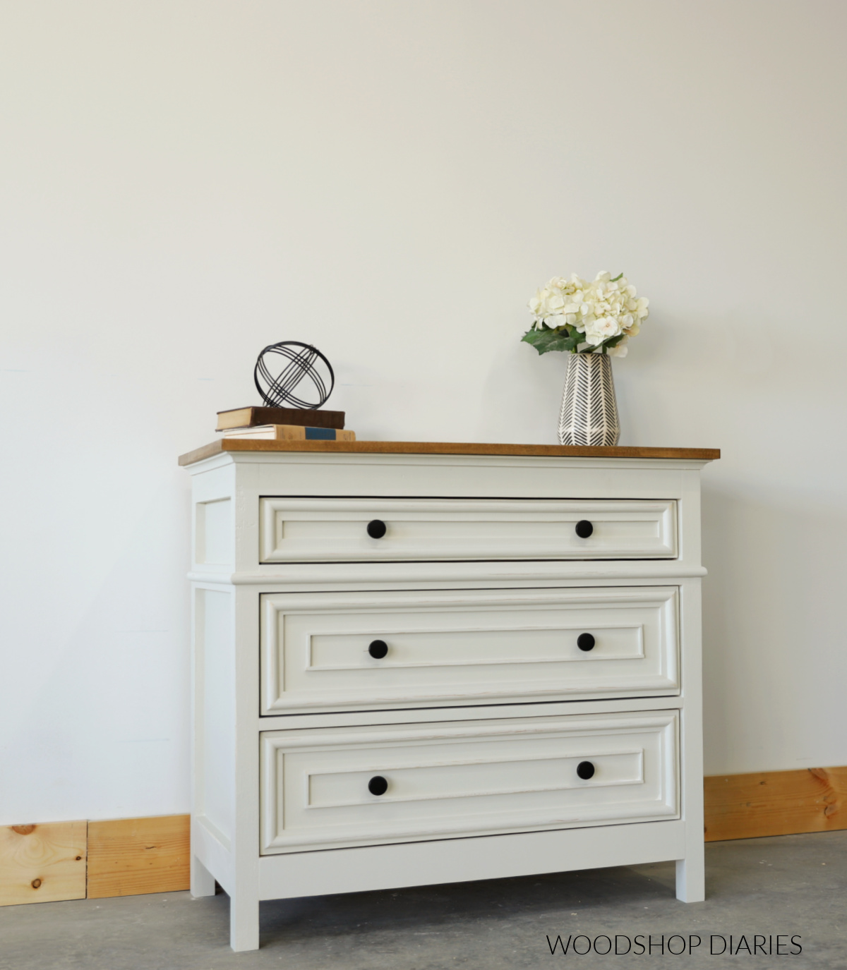 White and wood 3 drawer oversized nightstand with decorative trim along drawer fronts with black knobs