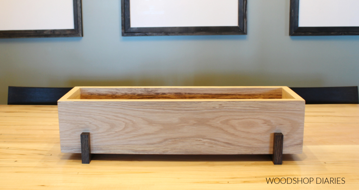 Wooden centerpiece box sitting on risers on dining table empty