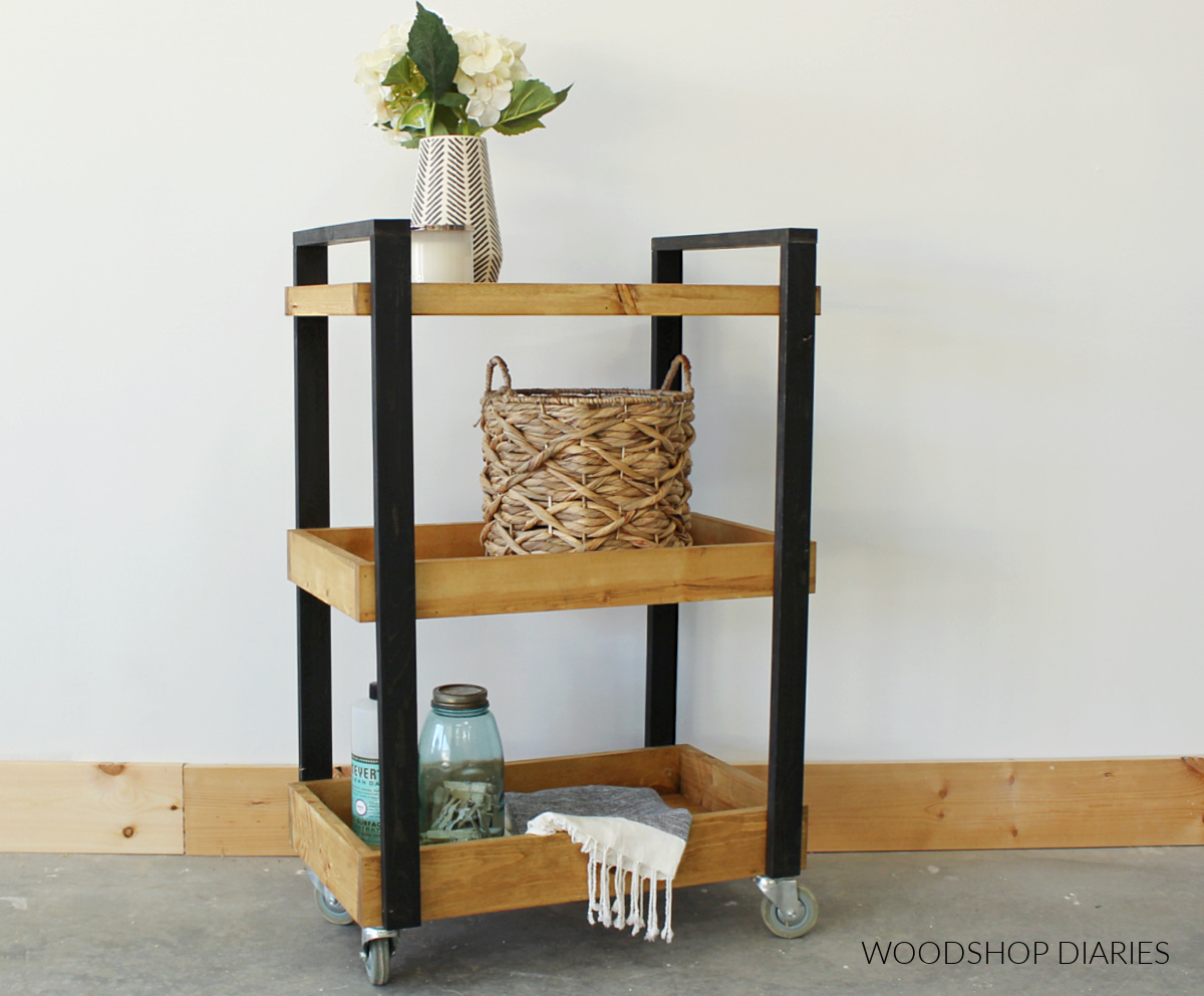 Completed two tone DIY rolling storage cart with wood stained shelves and black frame