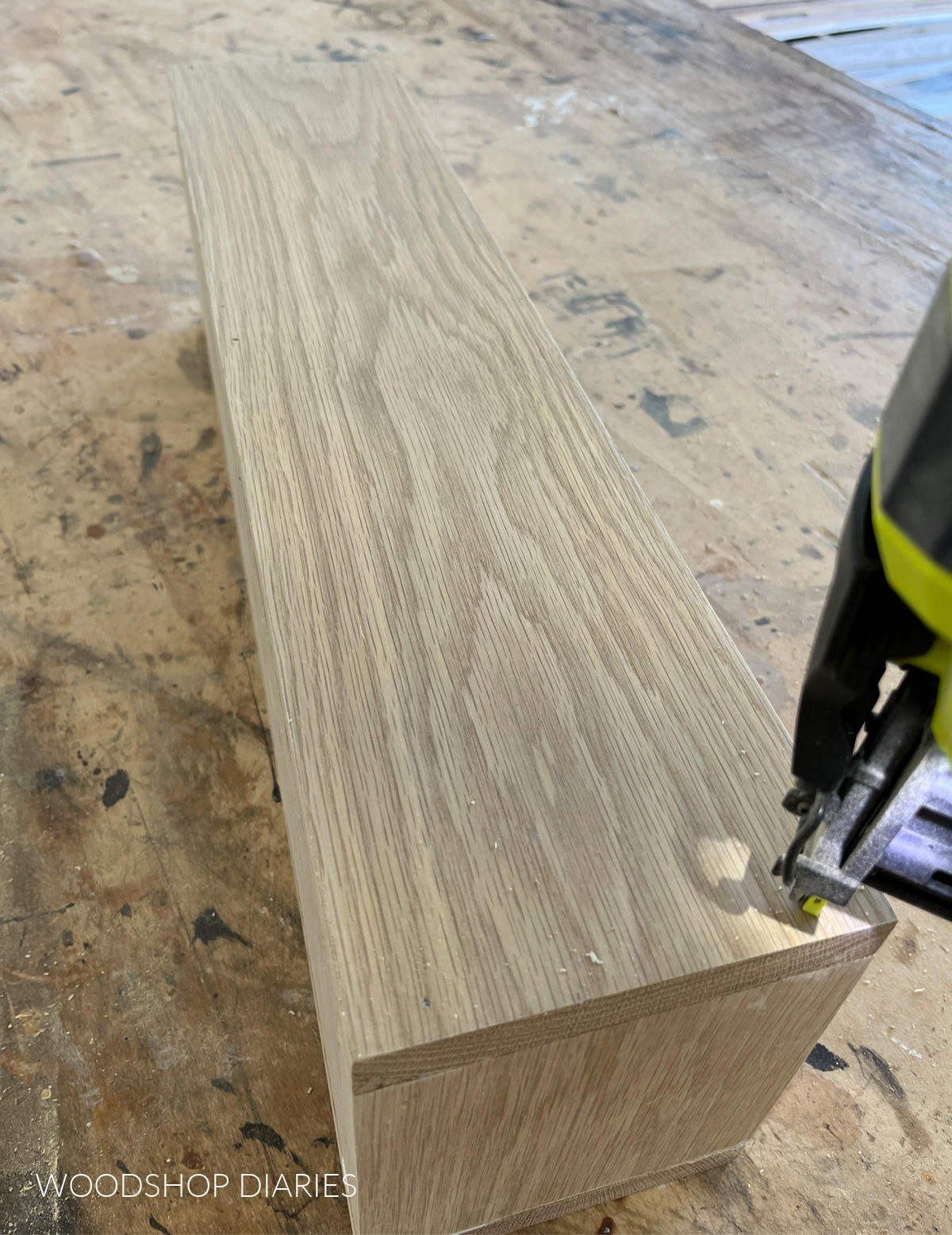 Close up of brad nailer securing long side to wooden box on workbench