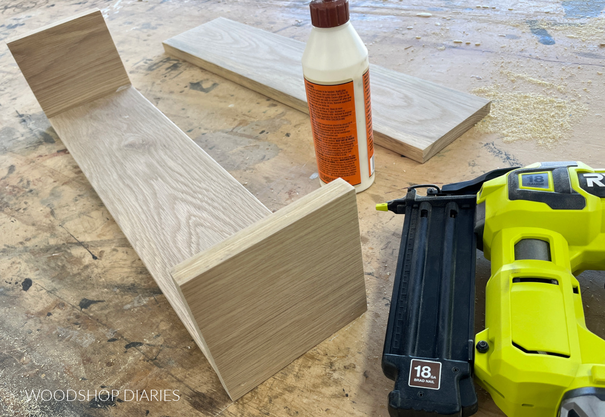 Brad nailer and bottle of glue sitting next to wooden box assembly with both sides attached