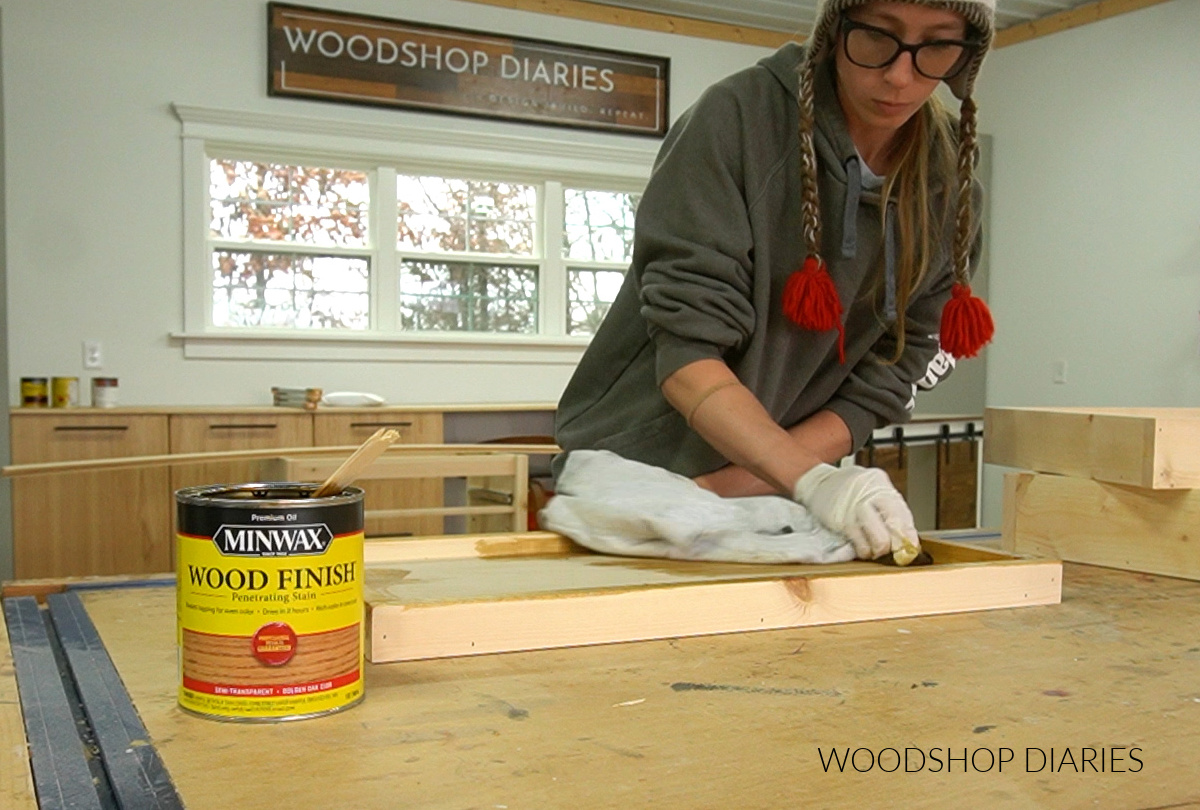 Shara Woodshop Diaries applying oil based wood stain to shelf with a rag