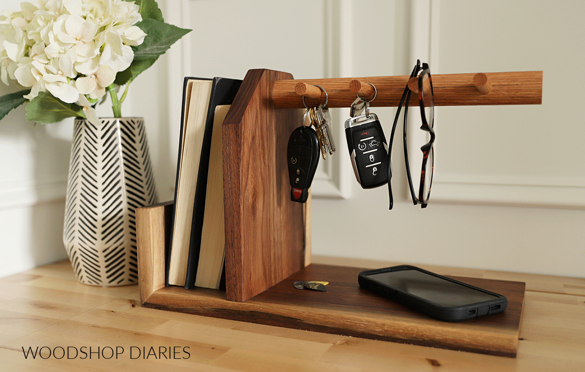 Walnut and red oak key holder catch all tray with pegs and bookends to contain books and mail sitting on wood surface next to vase with faux flowers
