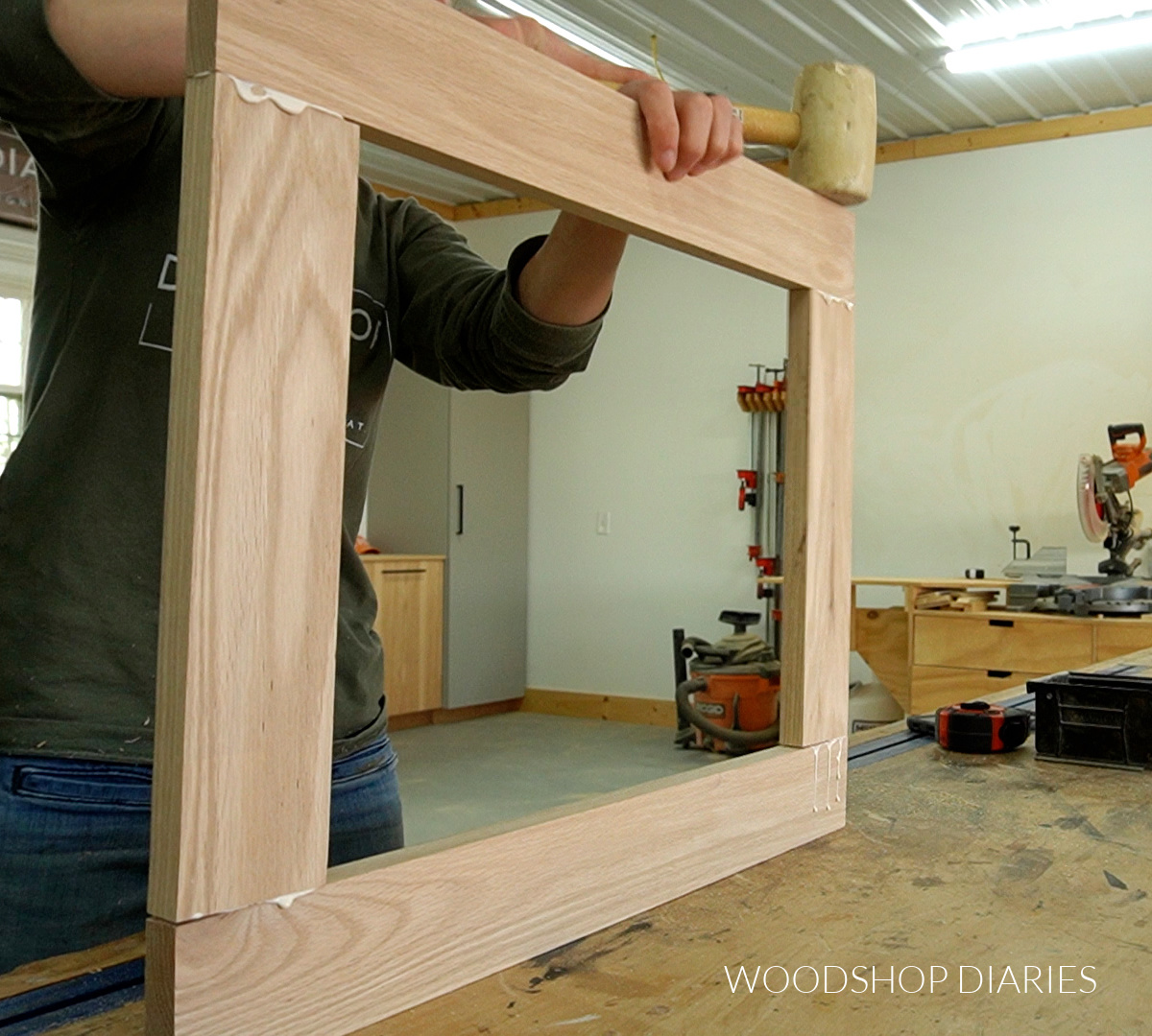 Using a rubber mallet to assemble door frame using dowels on workbench