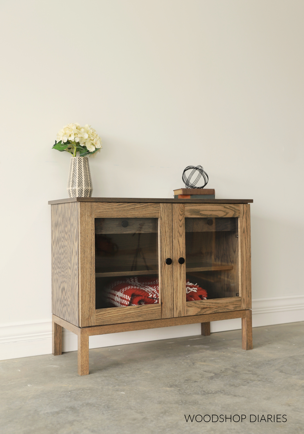 Red oak Glass door display cabinet with drawer and shelf against white wall stained Minwax Aged Barrel