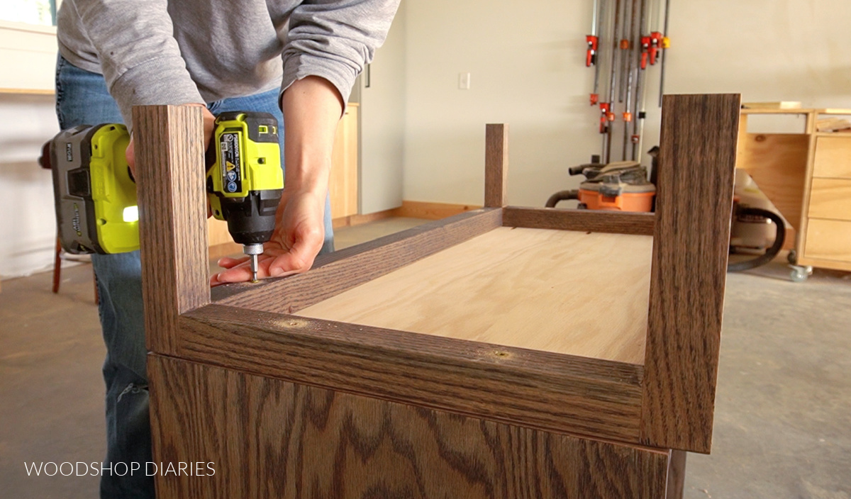 Using a drill to secure base to bottom of cabinet in workshop