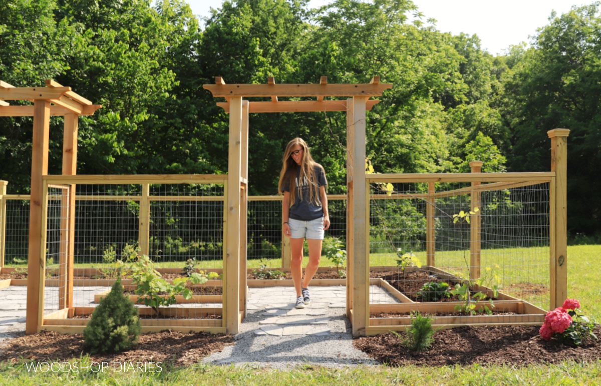 Shara Woodshop Diaries walking through garden arbor as entrance to fenced garden with pavers