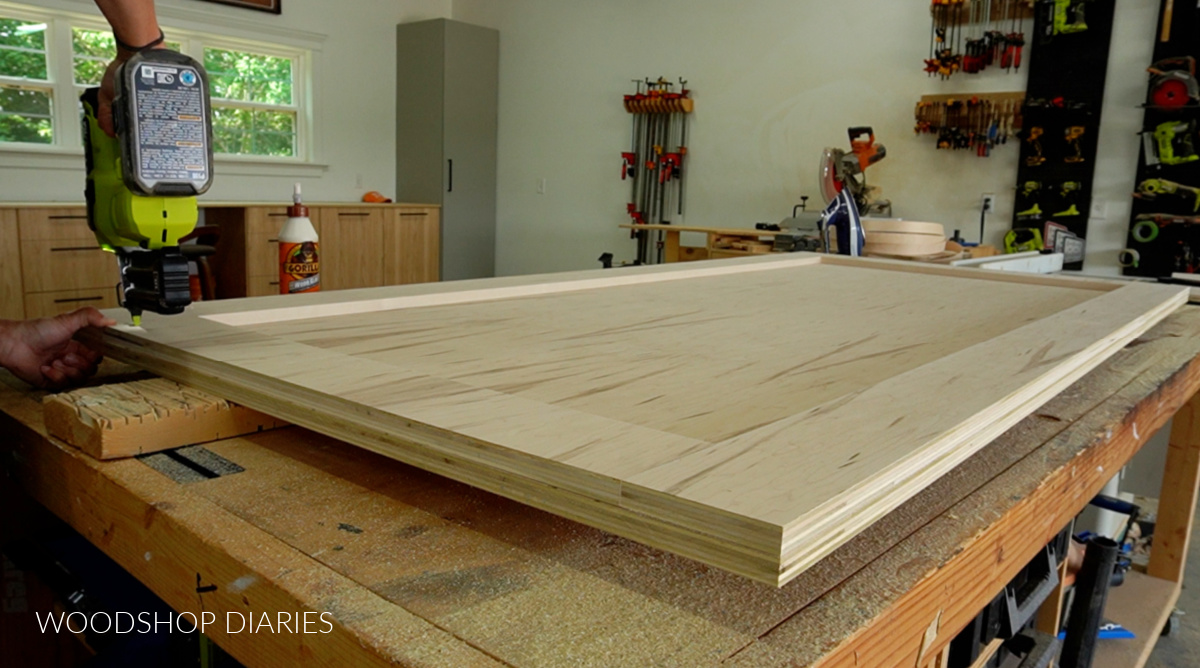 Shara Woodshop Diaries nailing trim on front of plywood door panel on workbench