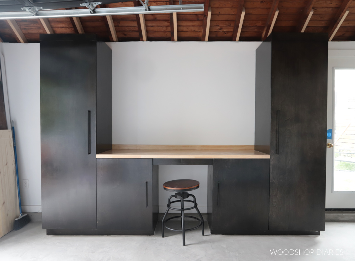 Black stained garage cabinets with butcherblock countertop against white wall