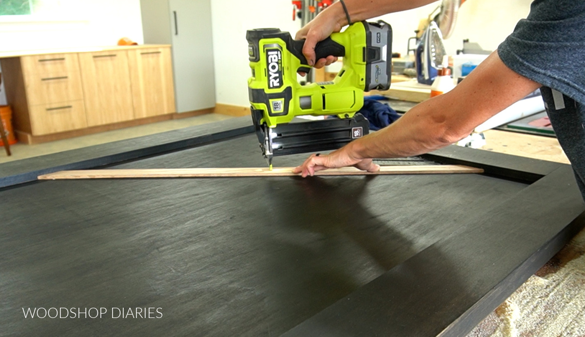 Using a brad nailer to attach diagonal wood slat on front of black stained sliding door