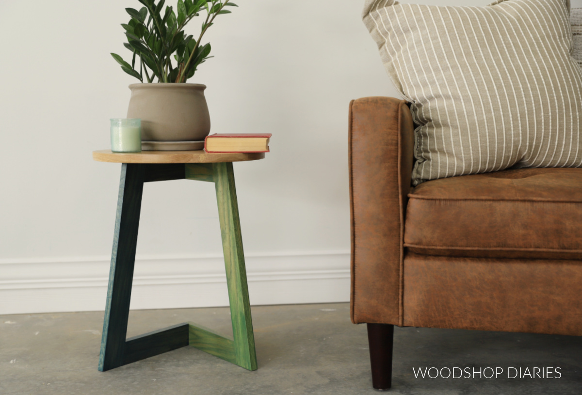 Modern C Table next to chair used as a side table with plant, candle and book on top