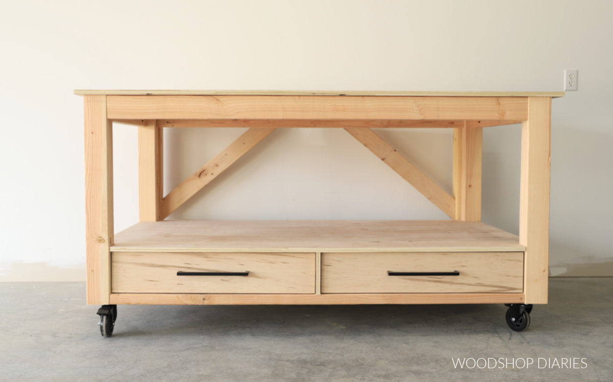 Completed DIY workbench with drawers at bottom and open shelving at top on caster wheels against white wall