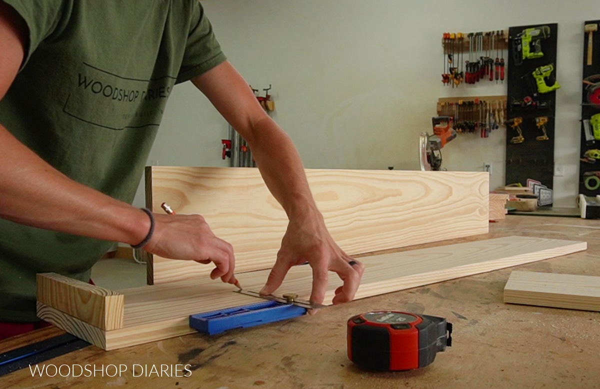 Shara Woodshop Diaries marking centerline of 1x8 back piece of plant shelf on workbench using Kreg MultiMark