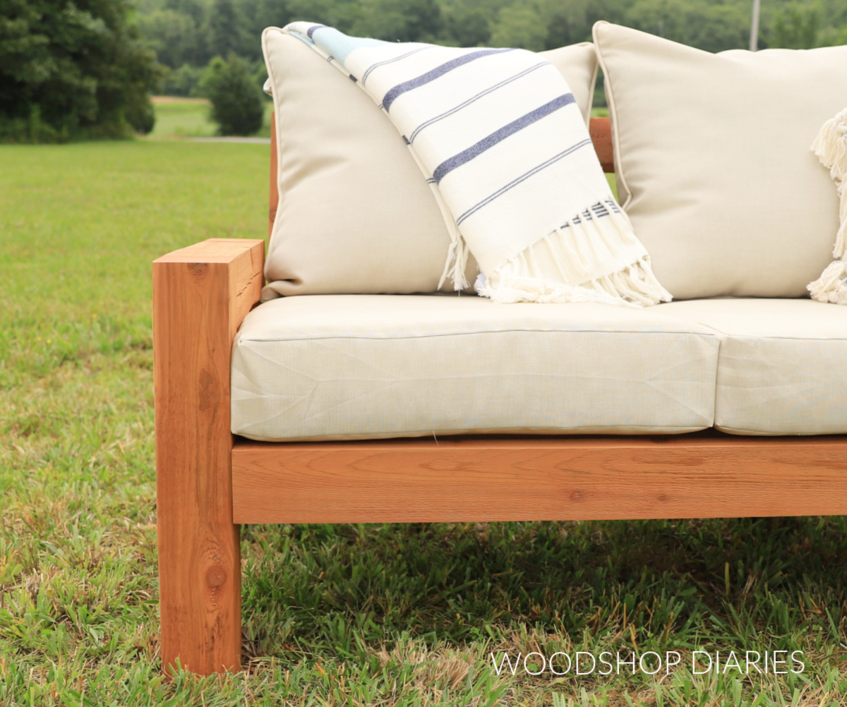 Close up of left side of wooden outdoor sofa with beige seat and back cushions
