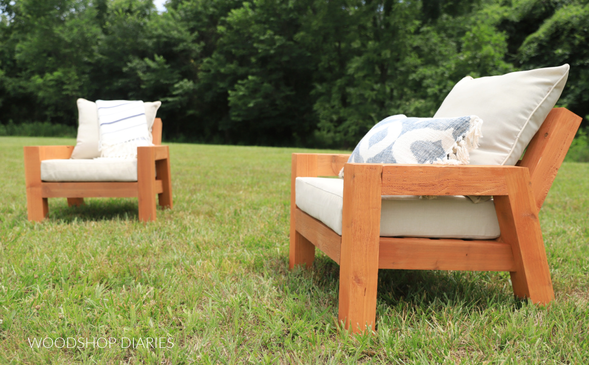 Two DIY wooden chunky style outdoor chairs with seat and back cushions in grassy area with trees in background