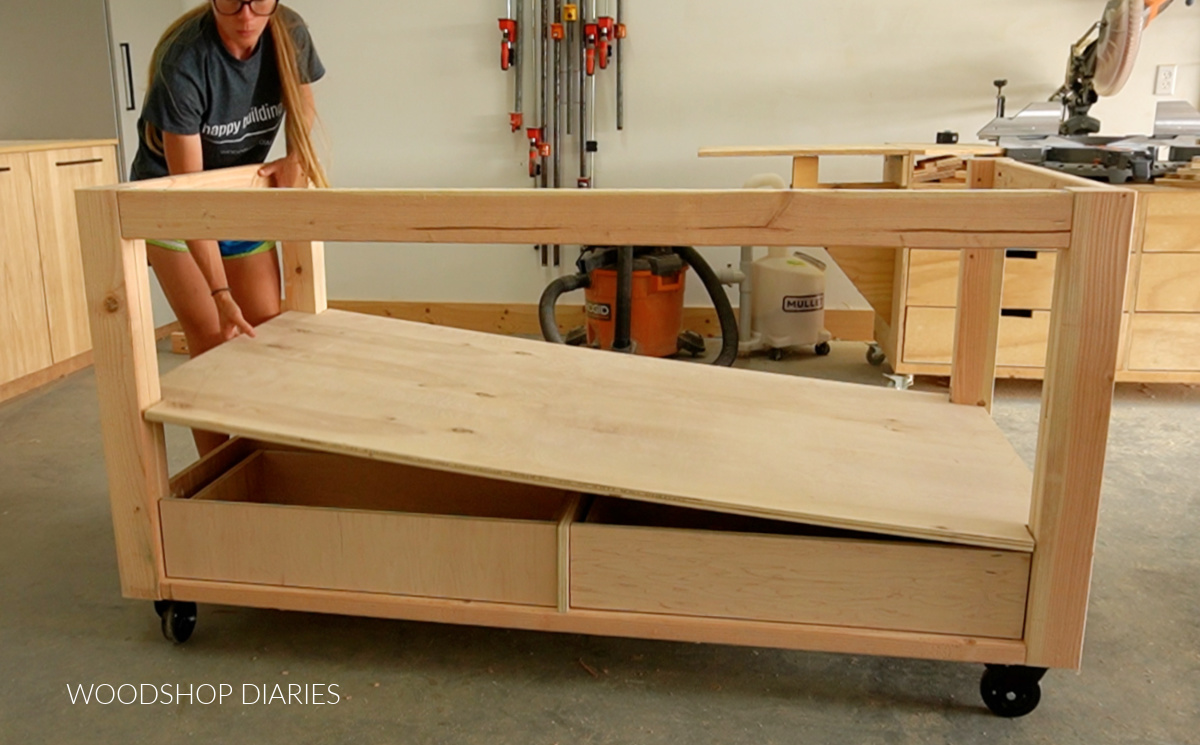 Shara Woodshop Diaries placing plywood panel onto drawer framing in workbench