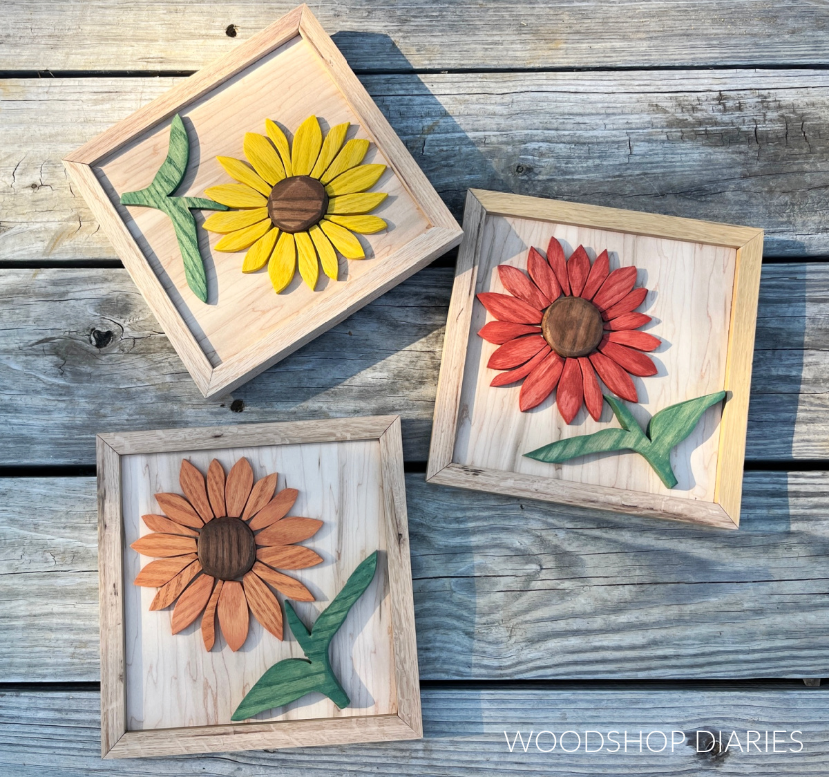 Three wooden sunflower art pieces against weathered wood backdrop--one yellow, one red, one orange flower