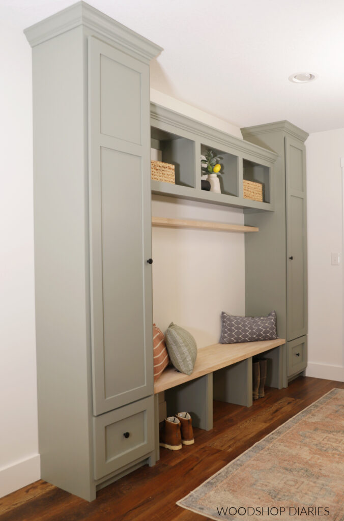 Built in mudroom cabinets painted SW evergreen fog against white wall--two tall cabinets, with bench and open cubbies between
