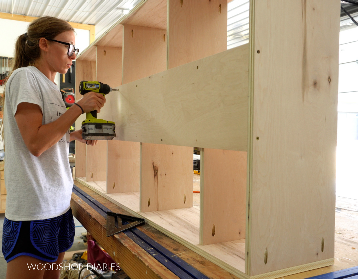 Shara Woodshop Diaries driving wood screws through back panel to secure individual shelves