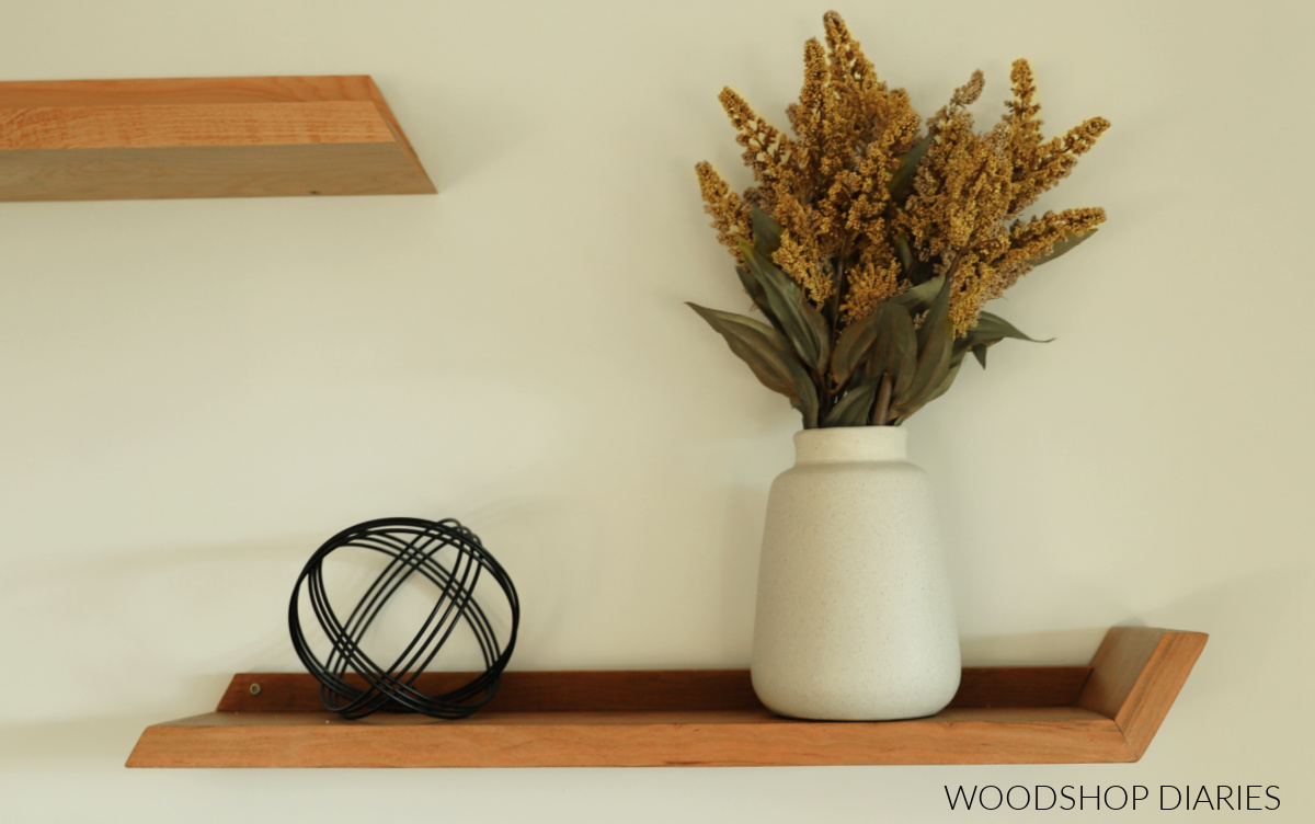 DIY wooden modern floating shelf made from cherry wood against white wall with vase and decor sitting on it