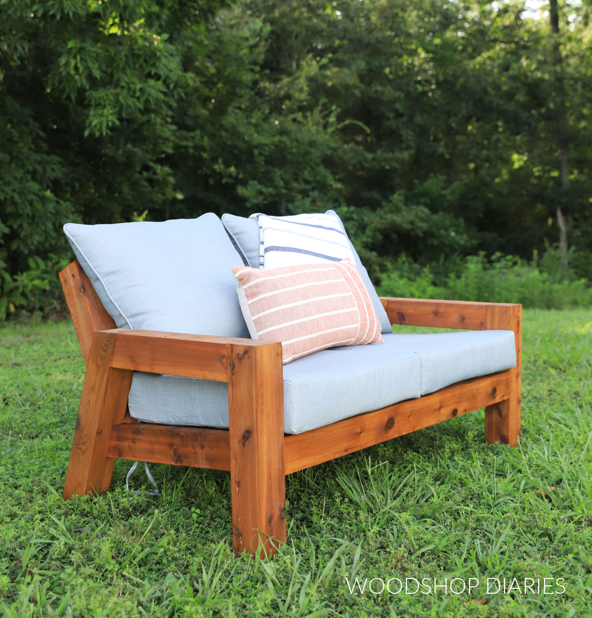 DIY cedar wood outdoor loveseat 2 seater sofa in grassy area with grey cushions and blanket