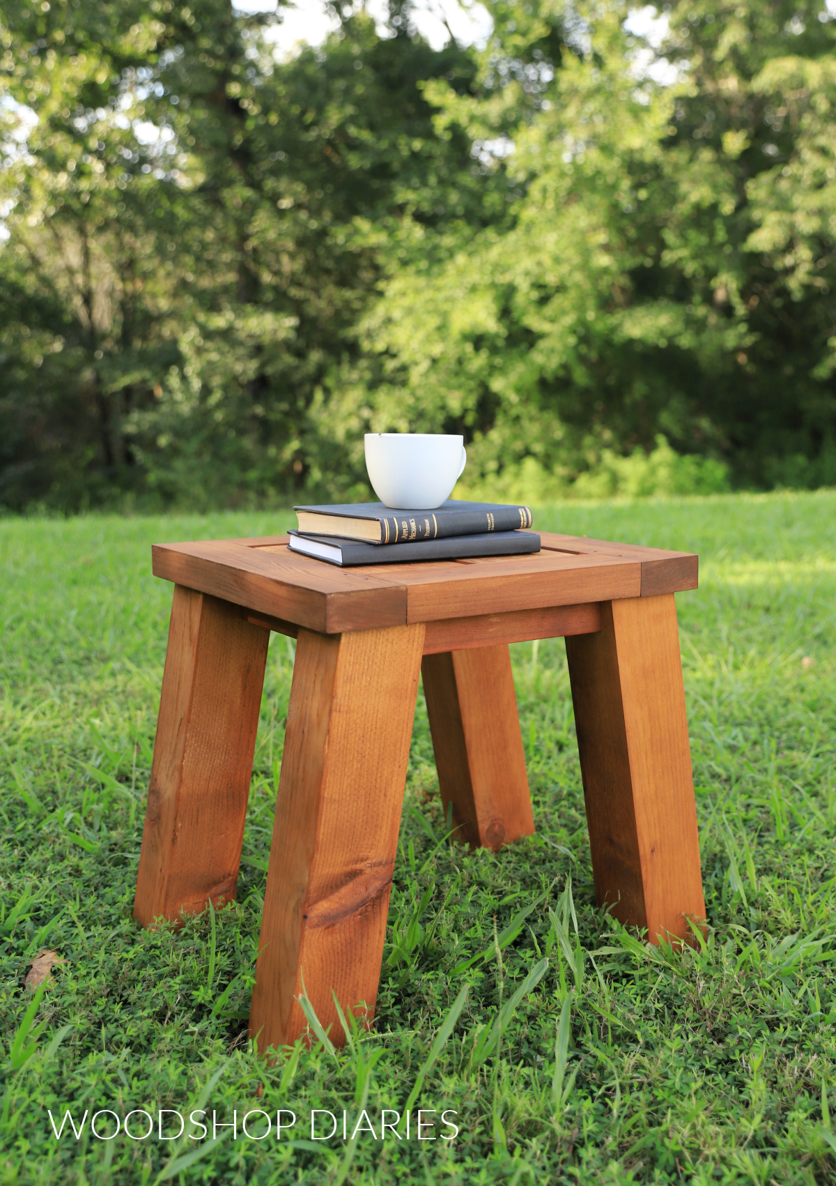 Simple wooden outdoor side table with books and mug on top sitting in grassy area outside