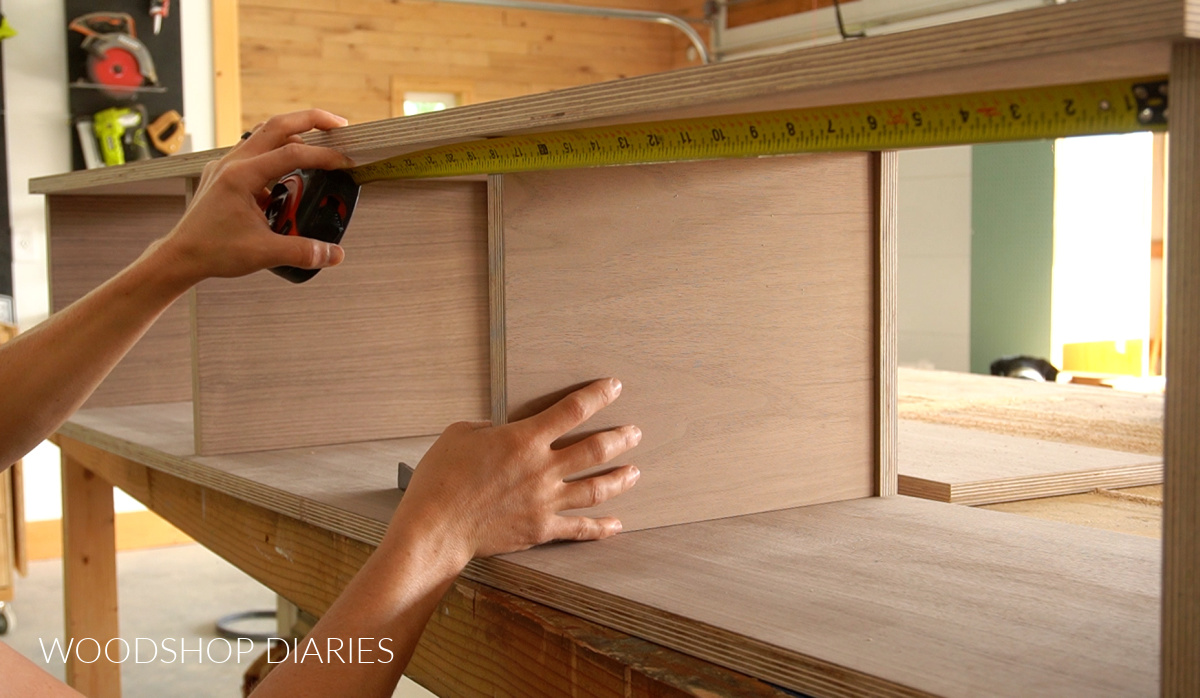 Shara Woodshop Diaries installing middle divider shelf into console cabinet with measuring tape