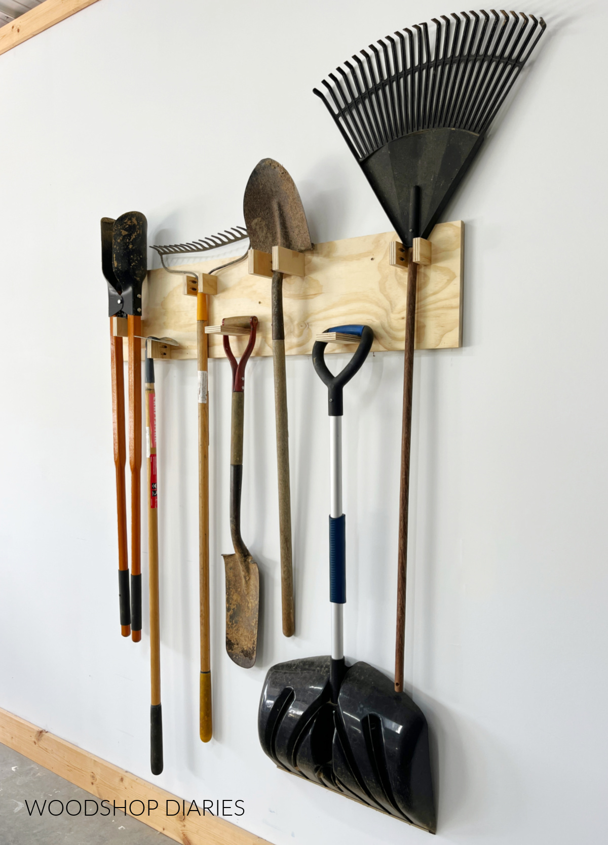 Completed yard tool organizer with shovels and rakes hanging on it against white wall
