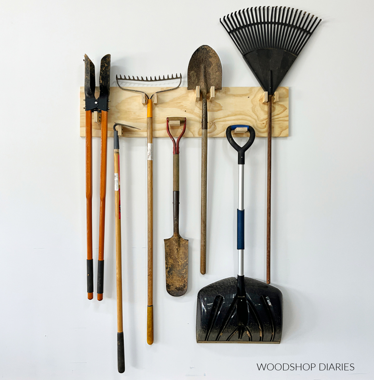 DIY Plywood yard tool organizer hanging on wall with shovels and rakes hanging on it