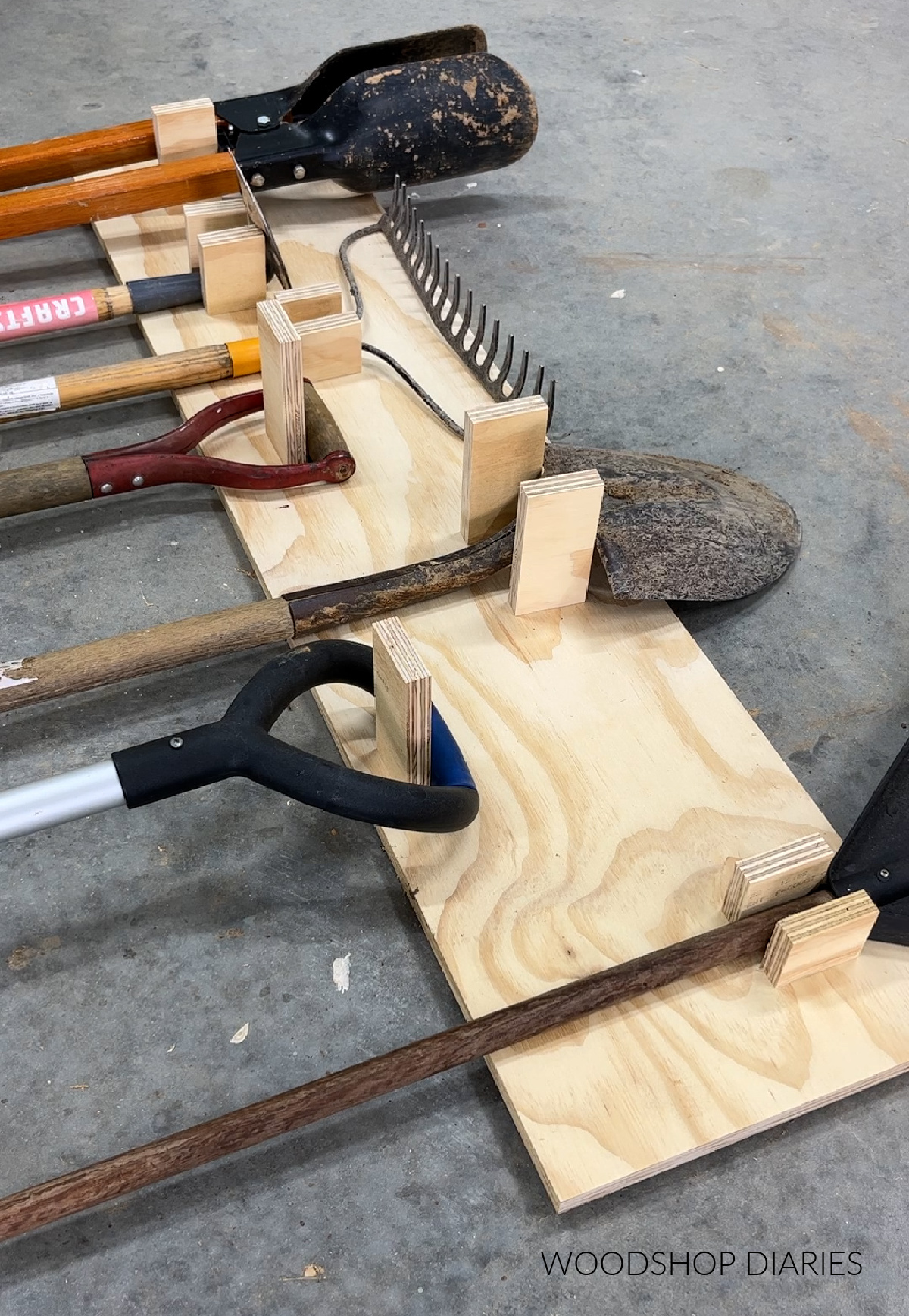 Yard tools laid out on plywood with hanger pieces cut to size under each tool