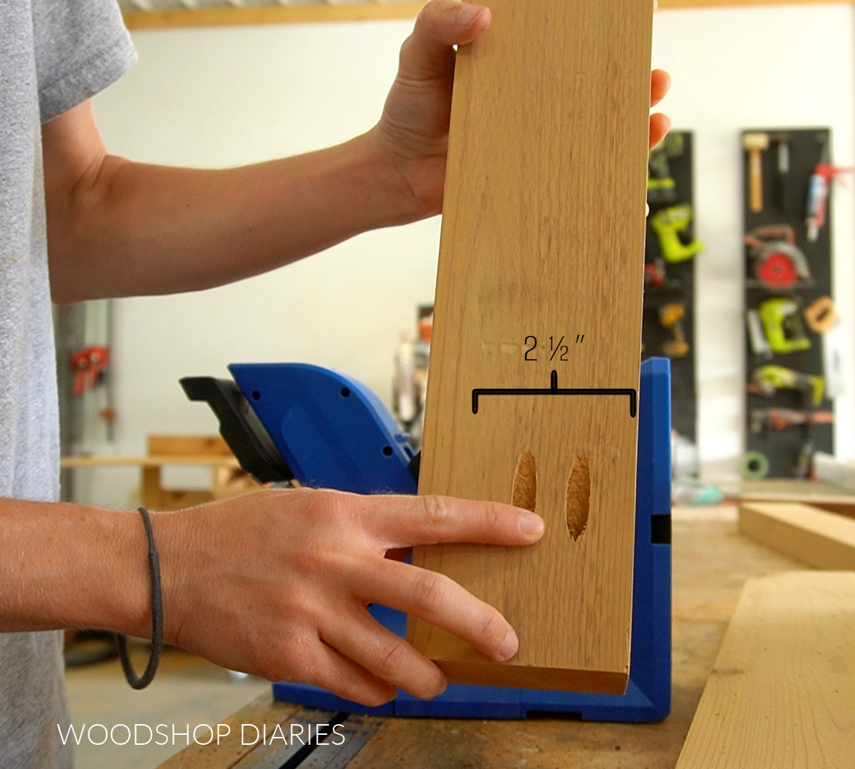Shara Woodshop Diaries holding 2x4 with pocket holes drilled into the end with bracket showing 2 ½" spacing where pocket holes are placed