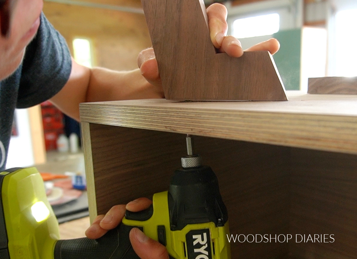 Shara Woodshop Diaries driving screws through bottom of mid century console cabinet to attach legs