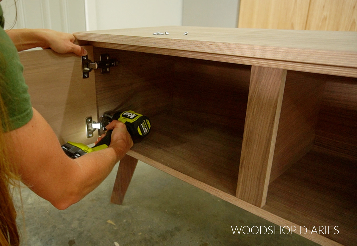 Shara Woodshop Diaries screwing door hinges into cabinet to install doors