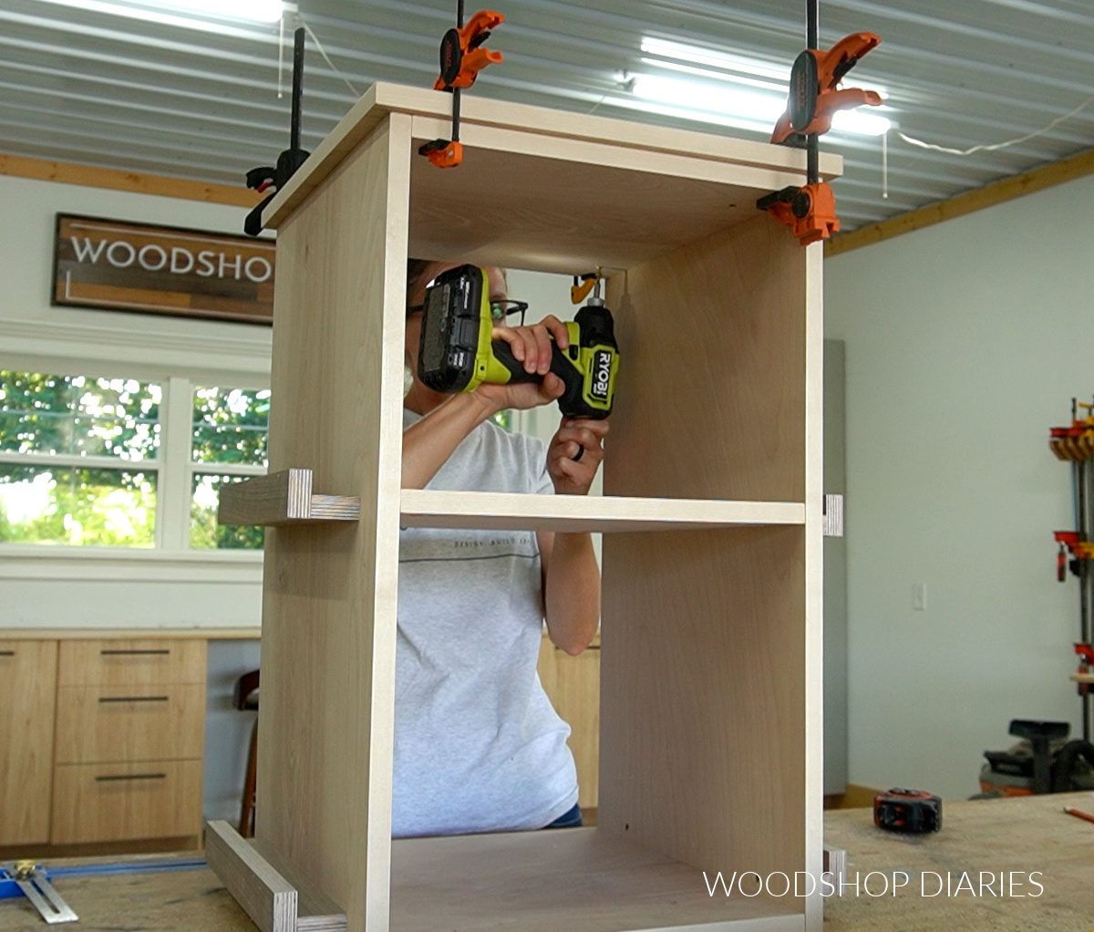 Shara Woodshop Diaries attaching top panel to rotating bookshelf with screws on workbench