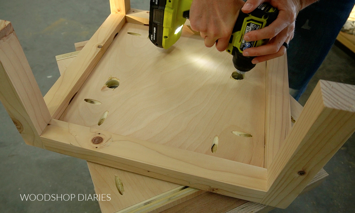 Driving screws through base access holes to attach lazy susan to bottom of bookshelf