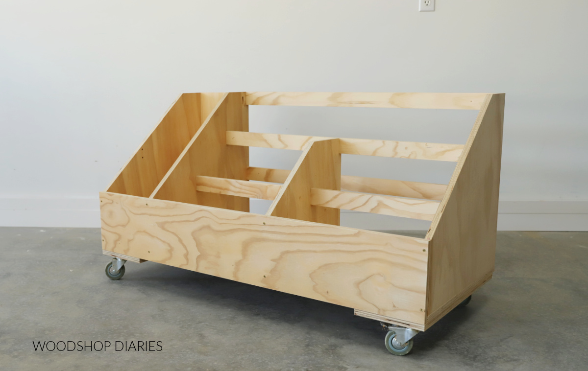 Empty scrap wood storage cart on caster wheels in workshop against white wall