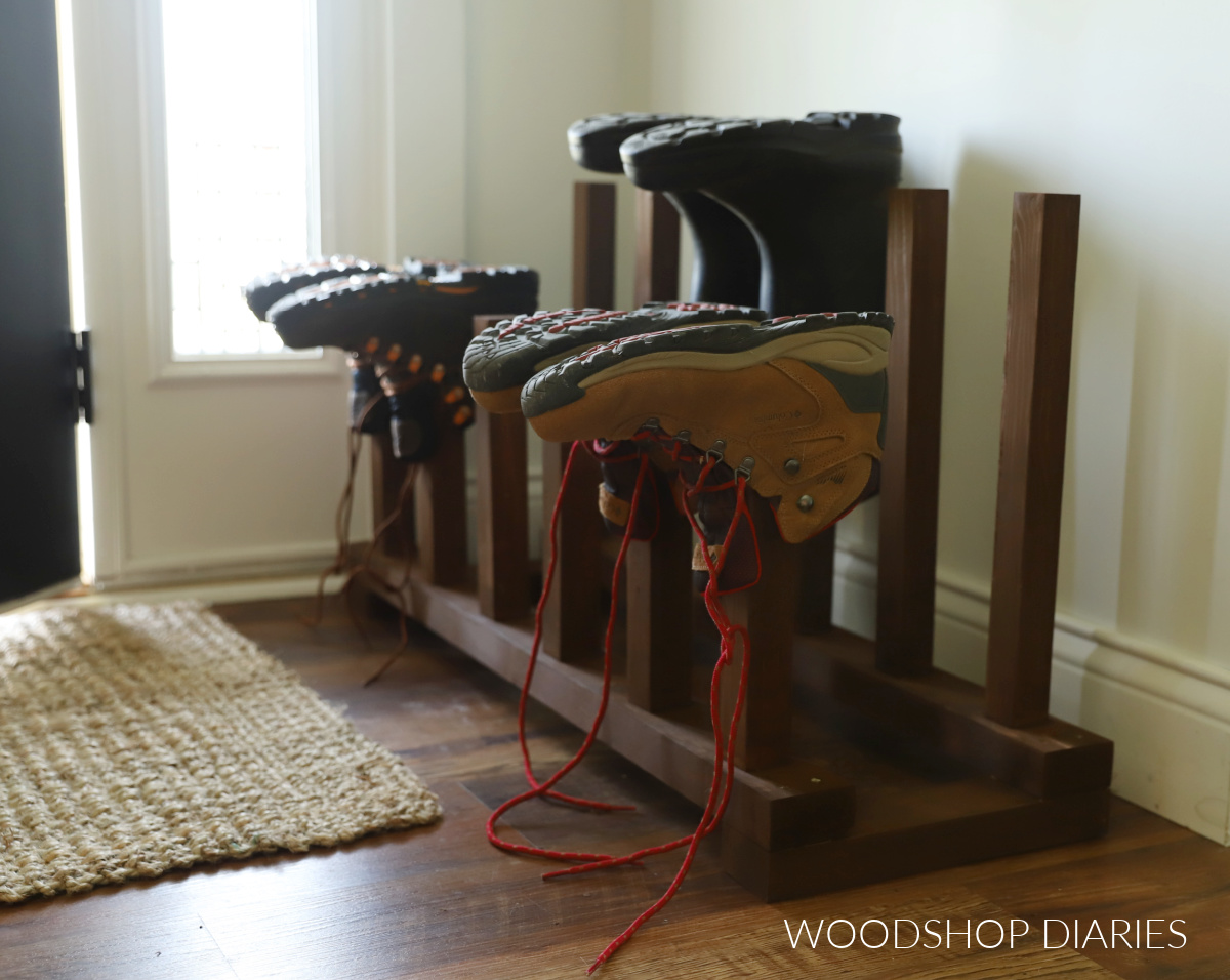 Completed scrap wood boot rack next to front door with rain boots and work boots on posts