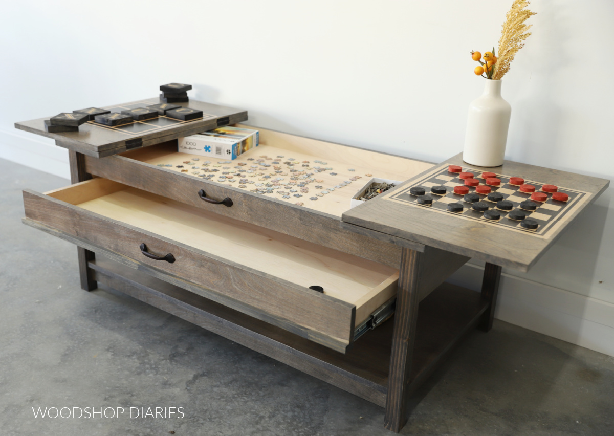 Puzzle coffee table with tops and drawer open. Puzzle partially completed in top compartment and tic tac toe and checkers being played on flip tops