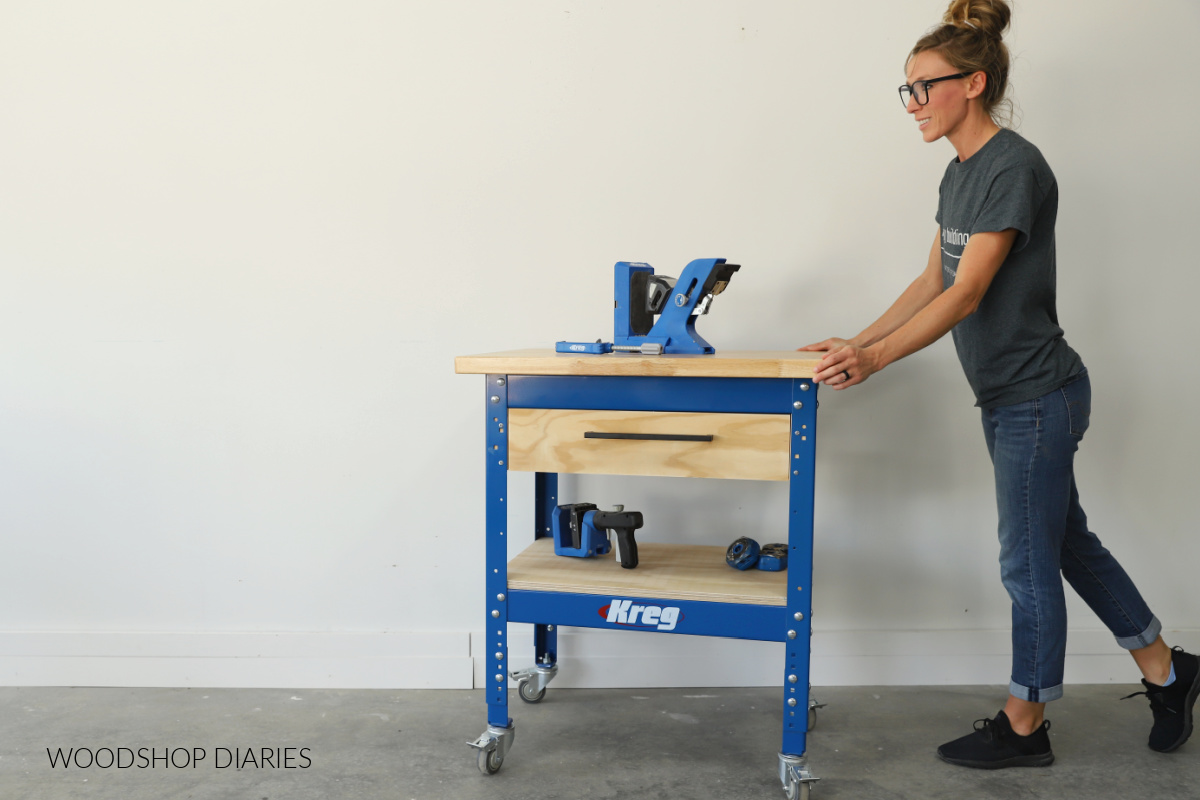Shara Woodshop Diaries pushing mobile workbench built on Kreg Universal Workbench frame with drawer and open shelving