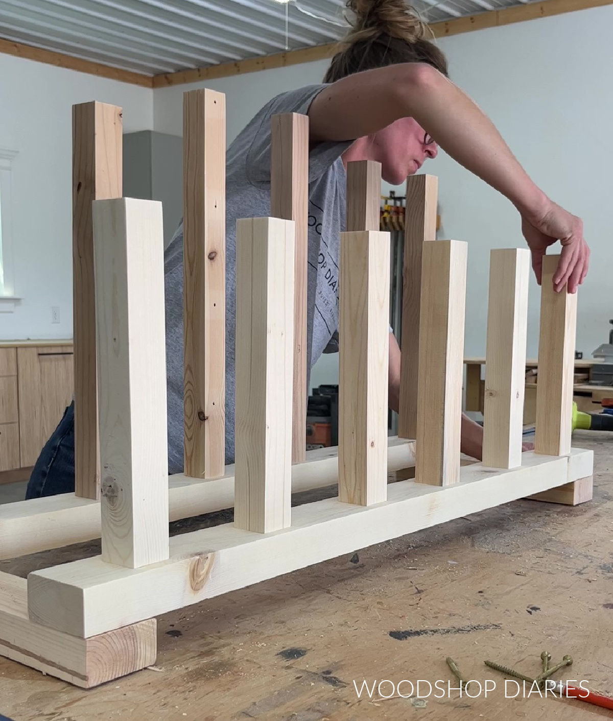 Shara Woodshop Diaries placing boot racks across base pieces on workbench