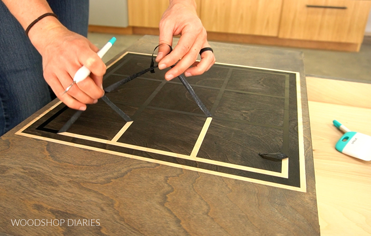 Removing vinyl stencil from table top to reveal tic tac toe board