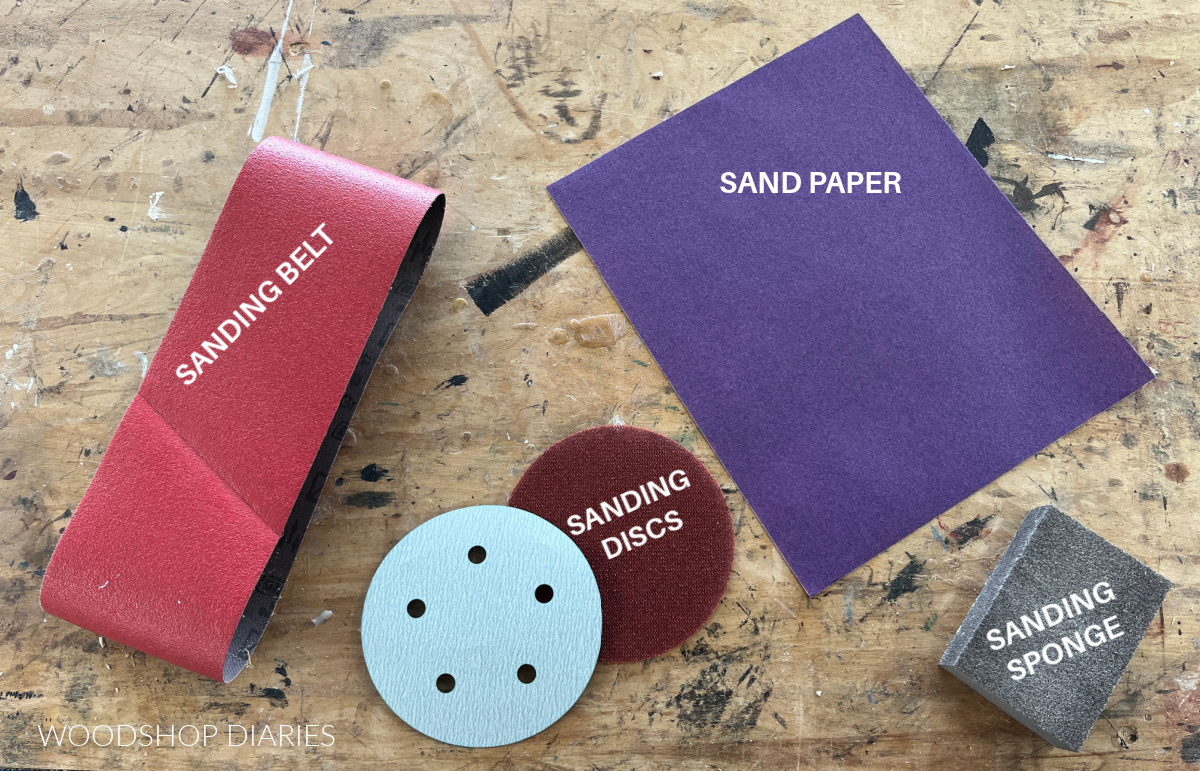 sanding belt, sand paper, sanding discs and sanding sponge laid out on workbench