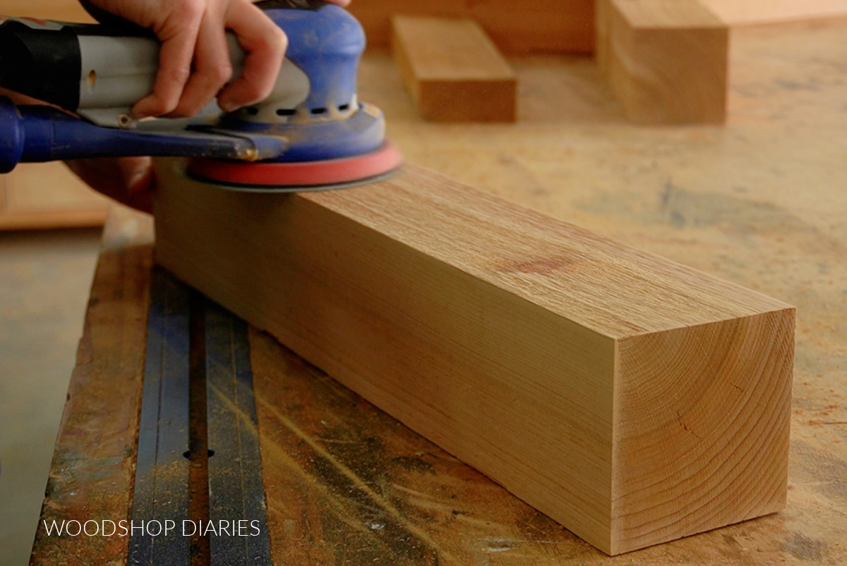 Orbital sander sanding rough cedar 4x4 on workbench