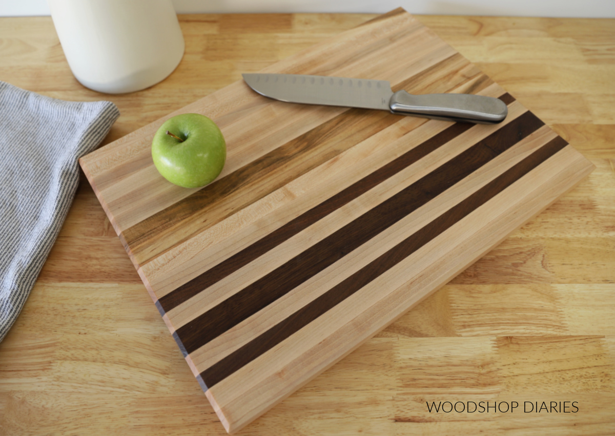 maple and walnut cutting board with apple on wooden table top