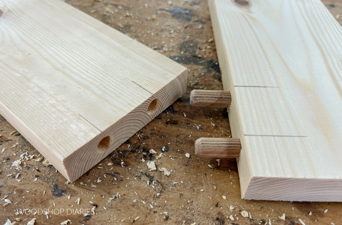 Close up of two boards with dowel holes drilled. Pins inserted into one of the boards showing alignment with the other